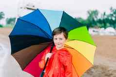 肖像微笑学校男孩彩虹伞公园孩子持有色彩鲜艳的伞肩膀快乐的孩子红色的雨衣持有多色伞在户外