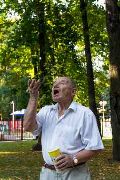 上了年纪的男人。走公园夏天养老金领取者高高兴兴地抛出爆米花玻璃捕获口宽开放
