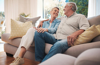 退休夫妇微笑沙发会说话的快乐婚姻养老金财富首页假期房子拥抱爱护理高级女人男人。放松沙发上生活房间夏天