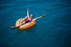 无忧无虑的年轻的女孩女人享受放松一天海浮动充气环前视图海假期概念