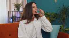 渴了年轻的女人坐着首页持有玻璃自然阿卡使口喝水
