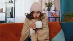 生病的年轻的女人穿他包装格子坐瑟瑟发抖冷沙发喝热茶