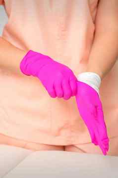 手美容师把无菌粉红色的手套准备收到客户在室内
