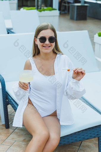 苗条的女人白色泳衣太阳镜说谎太阳懒人喝美味的鸡尾酒日光浴池夏天假期