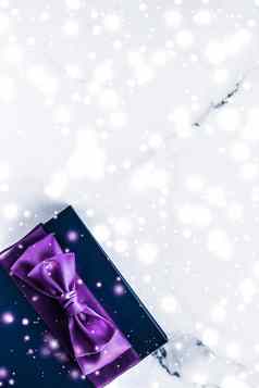 冬天假期礼物盒子紫色的丝绸弓雪闪闪发光的大理石背景圣诞节年礼物奢侈品美品牌平铺设计