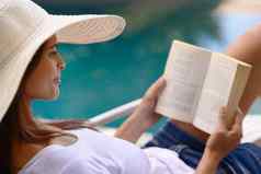 在游泳池边娱乐年轻的女人阅读书在游泳池边