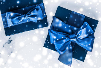 冬天假期礼物盒子蓝色的丝绸弓雪闪闪发光的大理石背景圣诞节年礼物奢侈品美品牌平铺设计