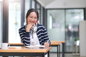 亚洲女人穿耳机移动PC咖啡馆写作笔记有吸引力的女学生学习语言看在线网络研讨会听音频电子学习教育概念