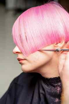 手理发师切割短粉红色的剪刀头发美容沙龙关闭一边视图