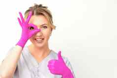 微笑医生眼科医生高加索人女人穿粉红色的橡胶手套统一的显示标志覆盖眼睛拇指手势白色背景