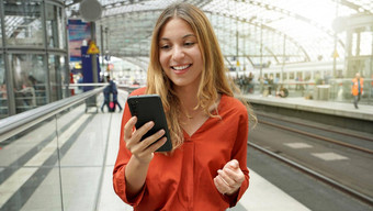 年轻的微笑女人持有移动电话太阳耀斑平台站旅行者女孩火车站手机数字无线网络互联网生活方式