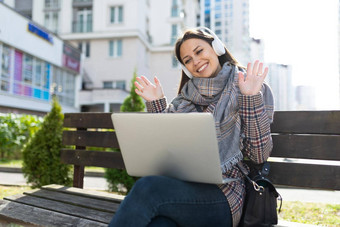 年轻的女人耳机移动PC沟通<strong>视频</strong>链接坐着街微<strong>笑脸</strong>