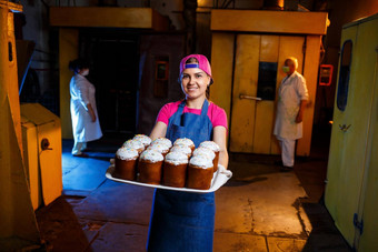 女孩贝克持有托盘热糕点面包店穿牛仔布连衣裙帽生产面包店产品架新鲜的脆皮糕点