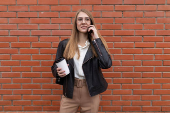 年轻的女<strong>学生会</strong>说话的移动电话杯咖啡手背景橙色砖墙