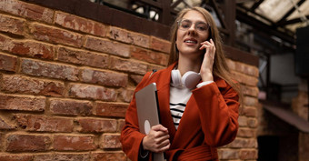 年轻的女人冲工作微笑脸移动PC手臂会说话的移动电话背景城市墙建筑