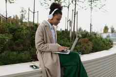 年轻的黑色的女学生准备考试工作移动PC在线耳机城市公园