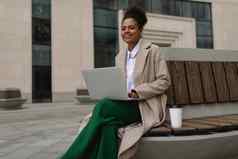 漂亮的成功的年轻的非洲美国女人工作移动PC在线坐着板凳上玻璃咖啡背景办公室建筑