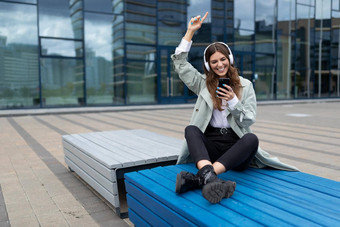 年轻的学生听音乐坐着板凳上瑜伽位置跳舞背景城市建筑