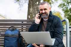 上了年纪的业务男人。说话移动电话工作移动PC在线公园板凳上