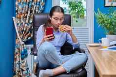 十几岁的女孩坐着扶手椅电脑智能手机吃零食