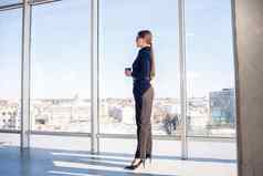 自信业务女人老板站现代办公室酒店窗口享受大城市视图女人领袖业务老板思考未来成功规划机会