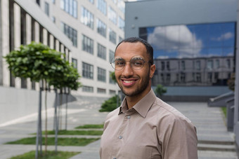 特写镜头照片肖像年轻的企业家穿眼镜拉美裔男人。微笑相机启动企业家现代办公室建筑