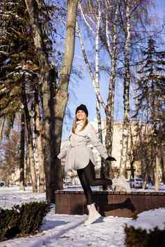 美丽的年轻的女人白色夹克白色皮革靴子走雪公园