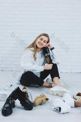 年轻的女人坐在地板上鞋子选择鞋子夫人白色衬衫黑色的裤子女人白色鞋子