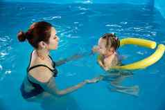 学前教育女孩学习游泳池泡沫面条年轻的教练