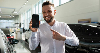 男人。车经销商演示了智能手机屏幕微笑