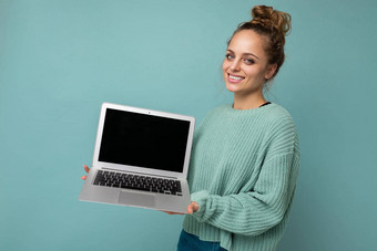 肖像照片年轻的不错的有吸引力的漂亮的积极的快乐微笑金发碧眼的女人真诚的情绪穿时尚的蓝色的毛衣孤立的蓝色的<strong>背景</strong>免费的空间持有移动PC电脑黑色的空白<strong>显示屏</strong>幕模型