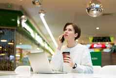 年轻的有吸引力的女人坐着购物中心表格工作电脑移动PC移动智能手机咖啡馆室内自由业务概念