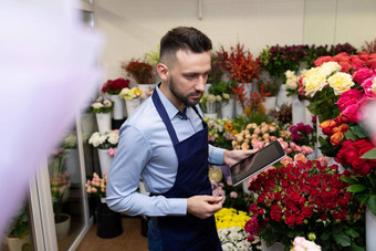 有魅力的男人。花店冰箱新鲜的花花束持有平板电脑手