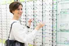 照片年轻的有吸引力的积极的微笑浅黑肤色的女人女人白色毛衣选择眼镜愿景商店窗口