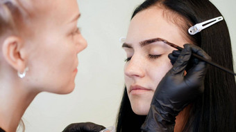 关闭年轻的女人眉修正过程美容师化妆艺术家适用于油漆刷眉毛美轿车专业护理脸