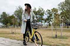 年轻的女人时尚的秋天衣服游乐设施自行车城市公园健康的生活方式概念