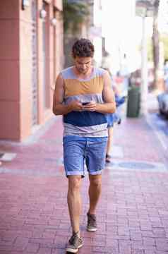沟通移动完整的长度拍摄年轻的男人。走城市街发短信手机