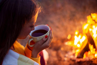 女孩喝温暖的茶坐着明亮的篝火