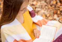 漂亮的整洁的女孩宽松的头发坐着板凳上秋天公园阅读书
