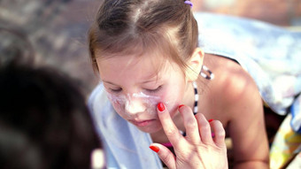 特写镜头孩子女孩严重的晒伤脸妈妈涂片的地方伯恩斯丰富特殊的奶油妈妈。应用太阳保护奶油女儿脸
