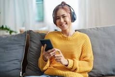 肖像年轻的亚洲女人女人耳机持有智能手机坐着沙发