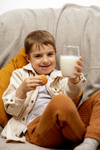 可爱的男孩坐着沙发上首页喝牛奶饼干新鲜的牛奶玻璃乳制品健康的喝医疗保健源钙乳糖学前教育孩子休闲服装