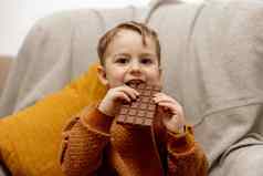 可爱的男孩坐着沙发上首页吃巧克力酒吧孩子糖果糖糖果孩子享受美味的甜点学前教育孩子休闲服装积极的情感