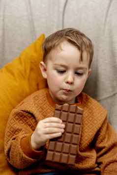 可爱的男孩坐着沙发上首页吃巧克力酒吧孩子糖果糖糖果孩子享受美味的甜点学前教育孩子休闲服装