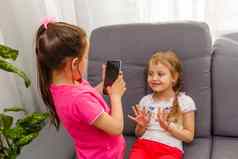 人孩子们技术朋友友谊概念快乐女孩坐着沙发采取自拍智能手机首页