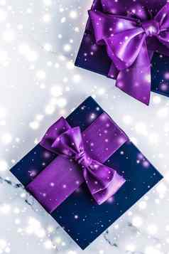 冬天假期礼物盒子紫色的丝绸弓雪闪闪发光的大理石背景圣诞节年礼物奢侈品美品牌平铺设计