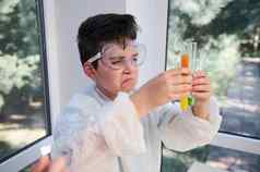 好奇的聪明的孩子男孩穿安全护目镜实验室礼服持有测试管看化学反应