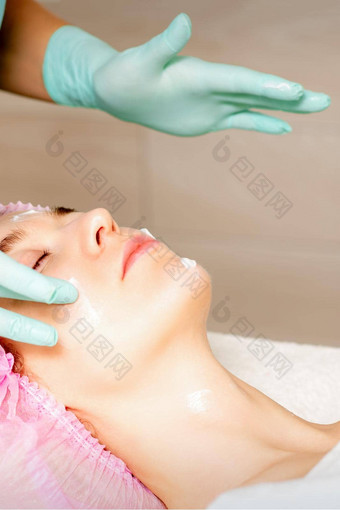 美容师戴着手套手适用于保湿面具剥奶油女脸<strong>面部</strong>美容治疗程序<strong>面部</strong>护理