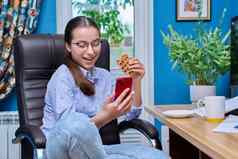 十几岁的女孩坐着扶手椅电脑智能手机吃零食