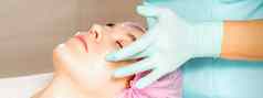 美容师戴着手套手适用于保湿面具剥奶油女脸面部美容治疗程序面部护理
